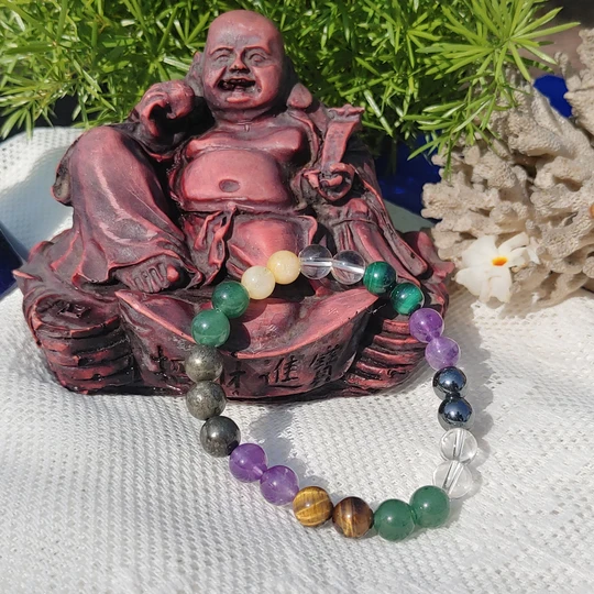 Laughing Buddha statue, reddish-brown, with a Money Magnet bracelet in foreground. Bracelet features amethyst, tiger's eye, clear quartz, Pyrite, citrine and other colorful healing crystals.