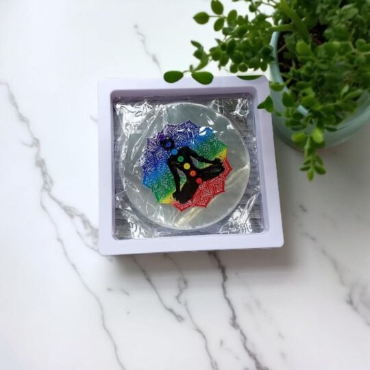 a white container with a colorful selenite plate in it placed on a white marble floor beside a plant